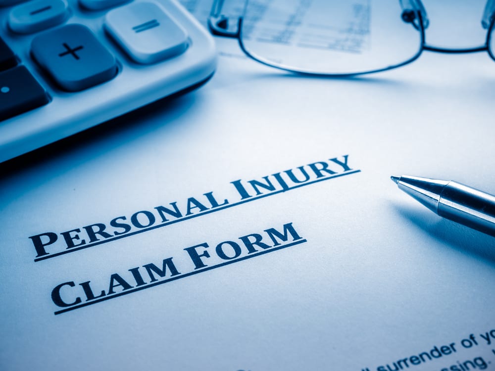 Personal Injury Claim form with calculator, pen, and glasses