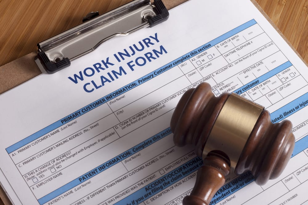 Work Injury Claim form on clipboard on table with wooden gavel