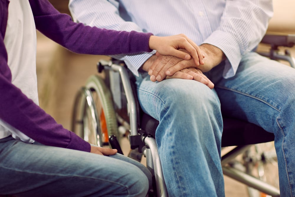 Man sitting in wheelchair holds hands with woman wearing a purple shirt