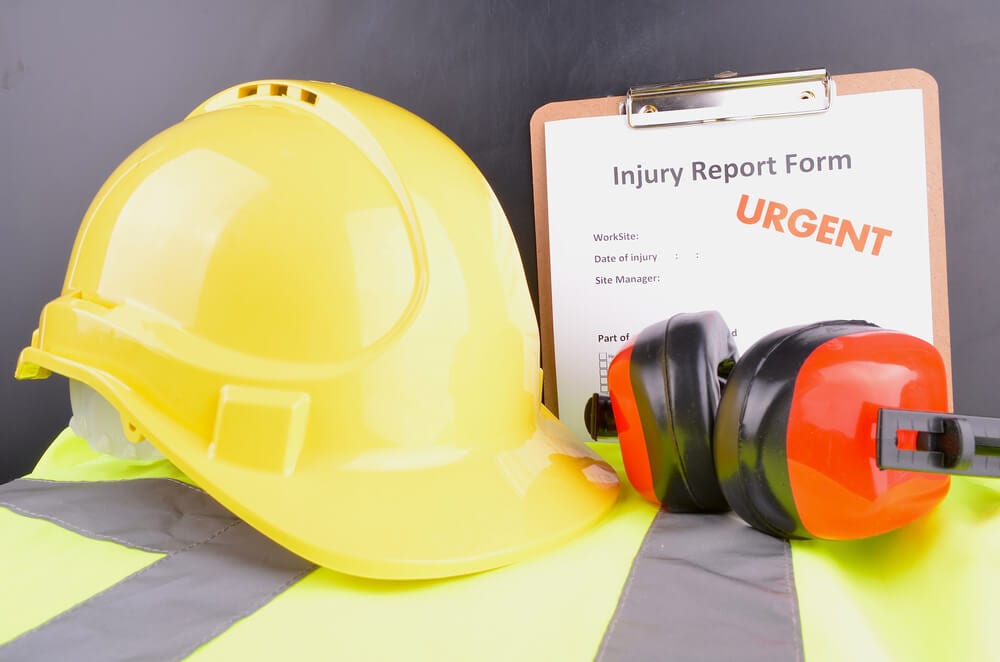 Yellow hard hat, orange ear protectors, yellow safety vest, and injury report form on a clipboard