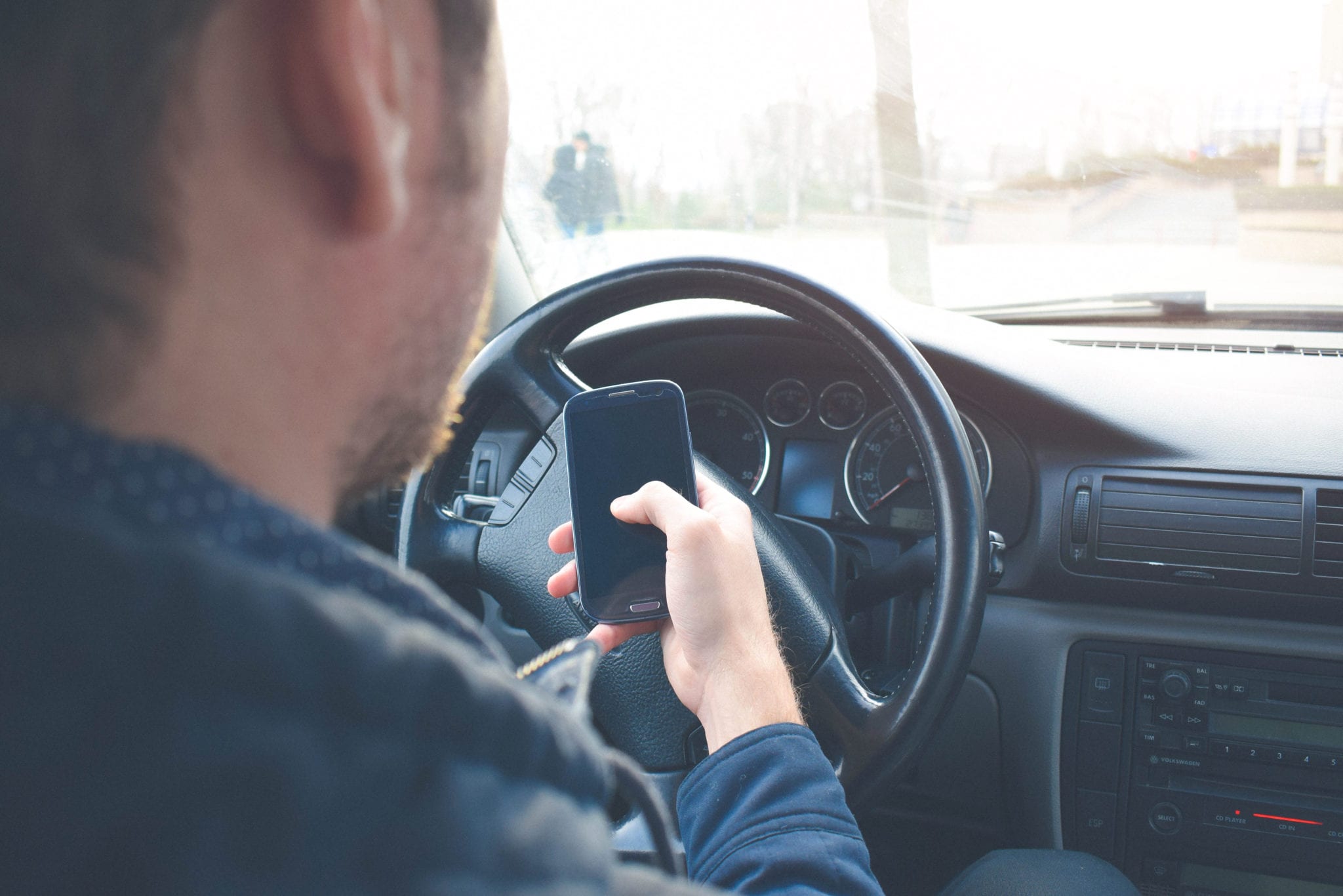 Man sitting behind wheel of car holding smart phone in one hand