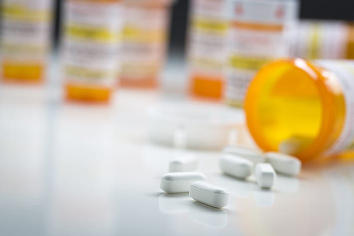 Orange prescription bottles on white table with white pills scattered around