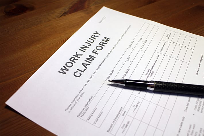 Work injury claim form paper on wooden table with black pen laid on top
