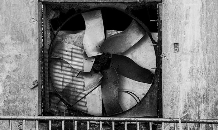 A broken metal industrial fan rests in an abandoned building